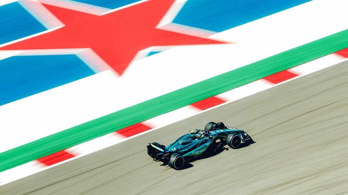 f1 Unauto da corsa Rivoluzione sfreccia lungo una pista ornata da una grande stella rossa e bordi blu e bianchi. LAston Martin scura, decorata con i loghi degli sponsor, manovra abilmente lungo i bordi definiti da linee rosse e bianche alternate.