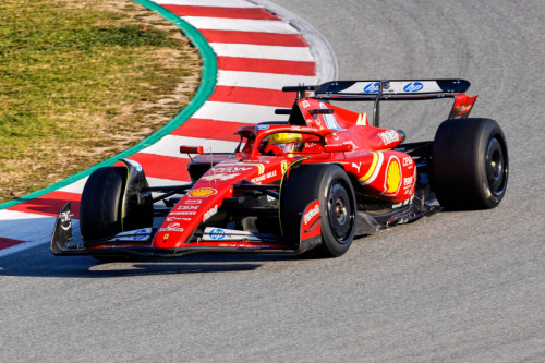 f1 Unauto rossa di Formula 1 che corre su una pista, con i loghi degli sponsor in evidenza. La pista ha cordoli rossi e bianchi e lo sfondo mostra un mix di asfalto ed erba. Il pilota indossa un casco e un equipaggiamento da corsa.